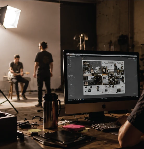 Bastidor de produção com set iluminado ao fundo e pessoa selecionando imagens no computador.