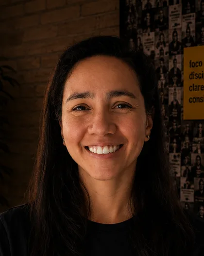 Integrante do time da Laeta de braços cruzados, camiseta preta, mural de fotografias atrás.