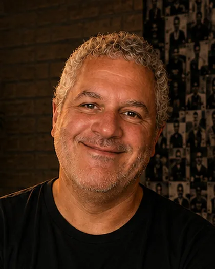 Integrante do time da Laeta grisalho, de braços cruzados, sorriso tranquilo, estante ao fundo.