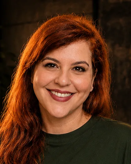Integrante do time da Laeta ruiva, de blusa verde, sorriso aberto, mesa de trabalho ao lado.