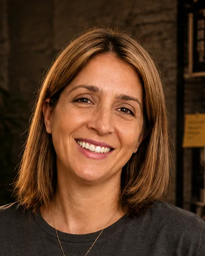 Integrante do time da Laeta de camiseta cinza e colar, sorrindo, estante de livros atrás.